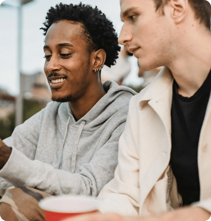 Two friends are watching the news on a smartphone. One young man has a cup of coffee in his hand.