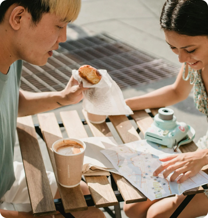 Woman in White Shirt with Brown Vest Drinking Coffee with a Man Seated in Front of Her